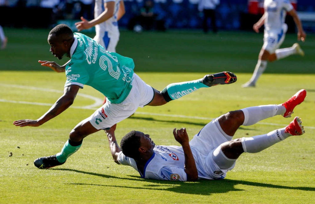 Mexico Liga MX Football - action of two players colliding; one player is laying on the ground, the other is jumping over him.